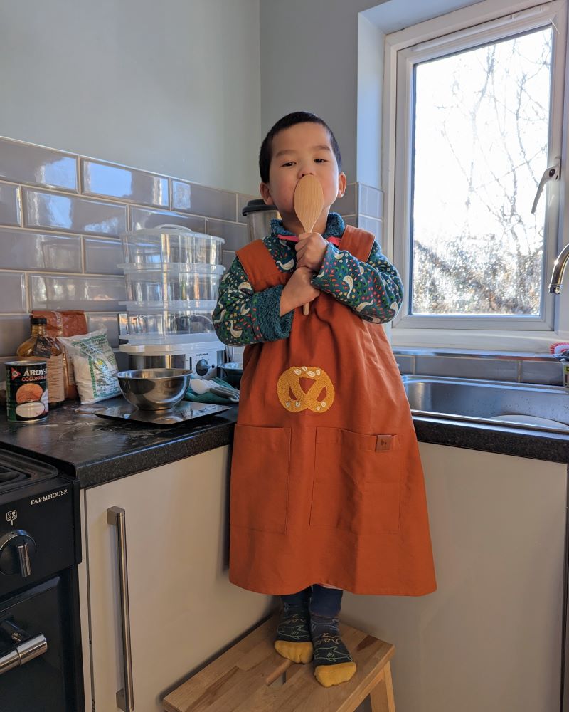 Liz's son in a Fabelab apron licking the wooden spoon used in baking new year's cake for her Lunar New Year celebrations