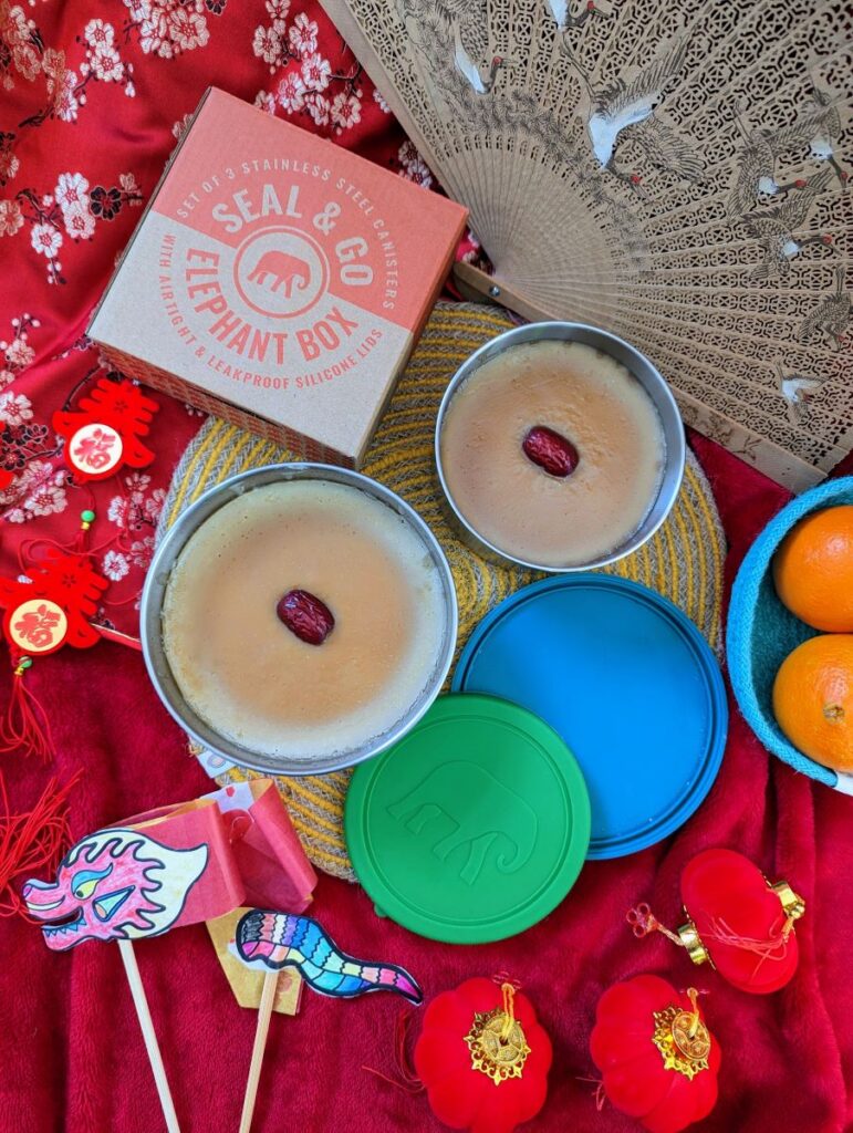 New Years cake in round tins on a yellow seagrass placemat, decorative red tablecloth and Lunar New Year decorations