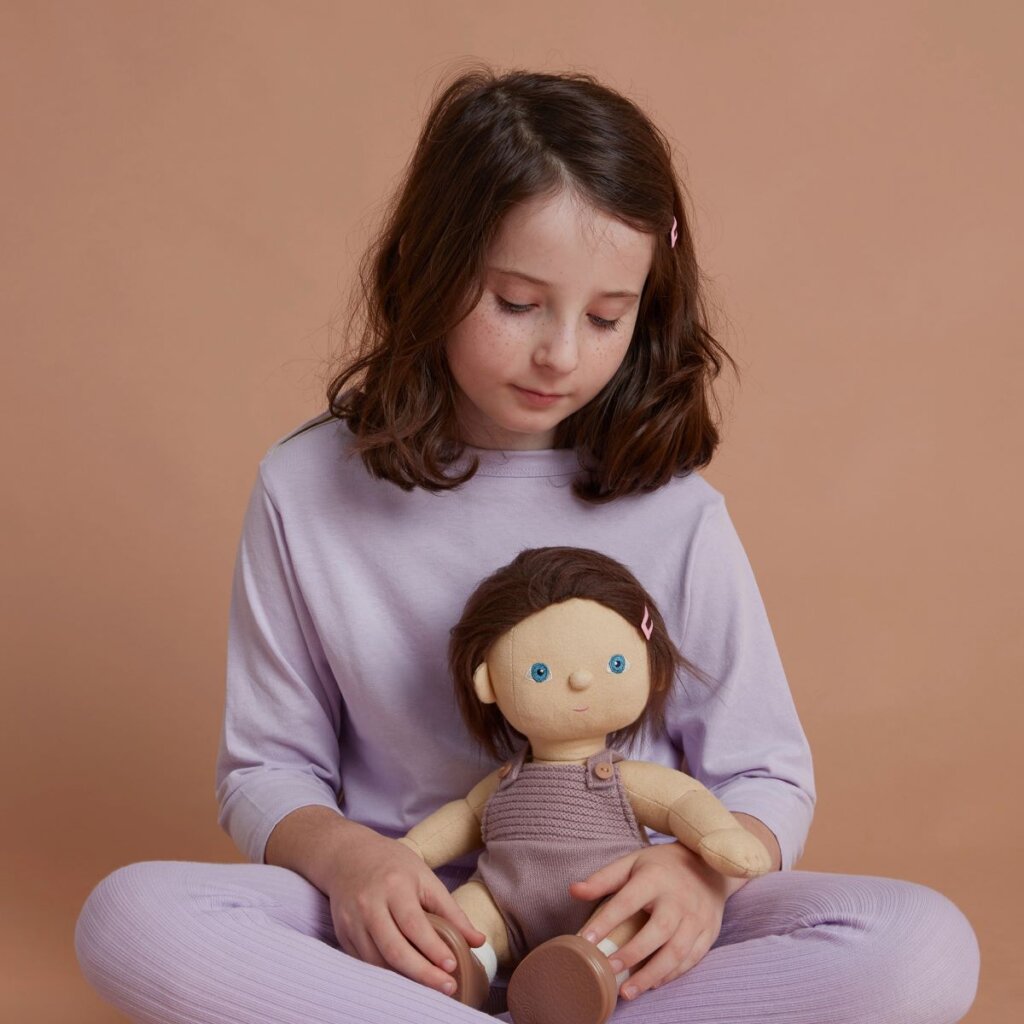 A child sat cross-legged holding Dinkum Doll Betsy in their lap