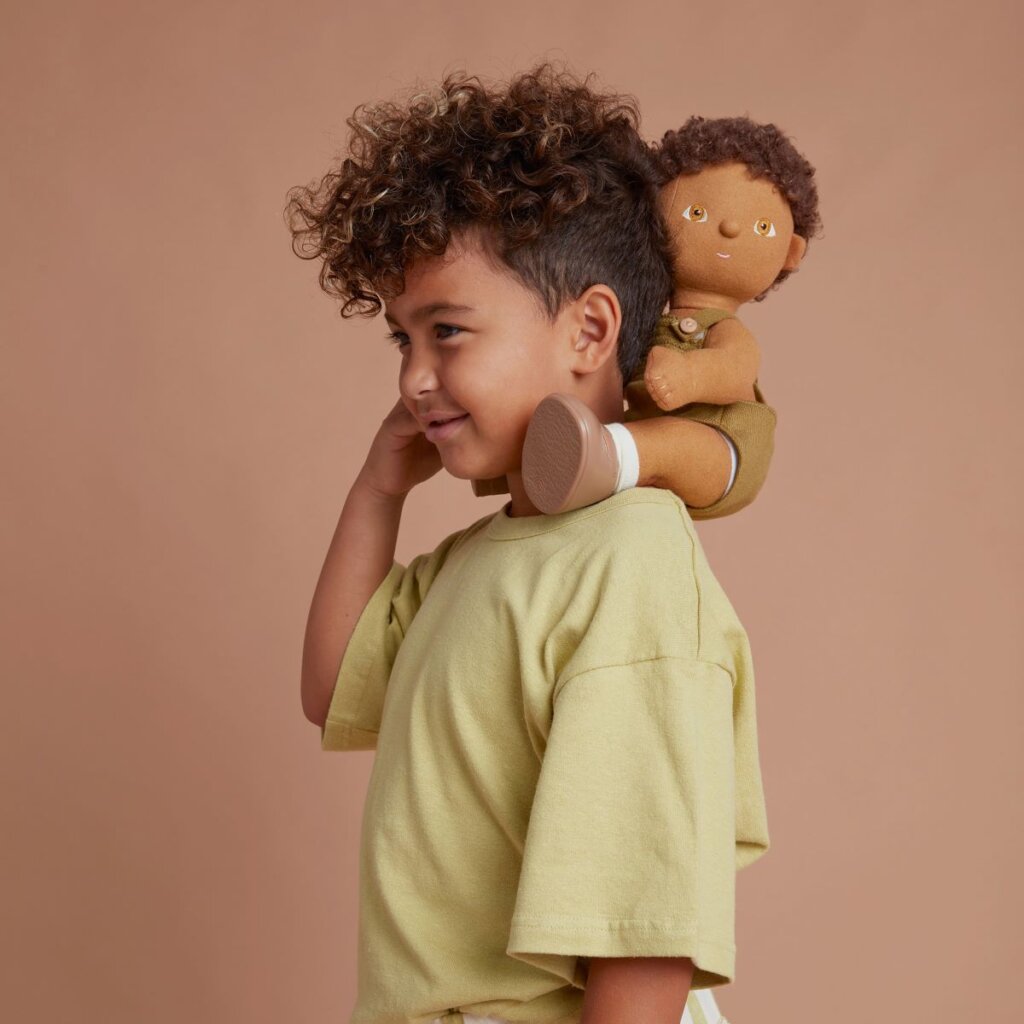 A child holding Dinkum Doll Button on their shoulders smiling