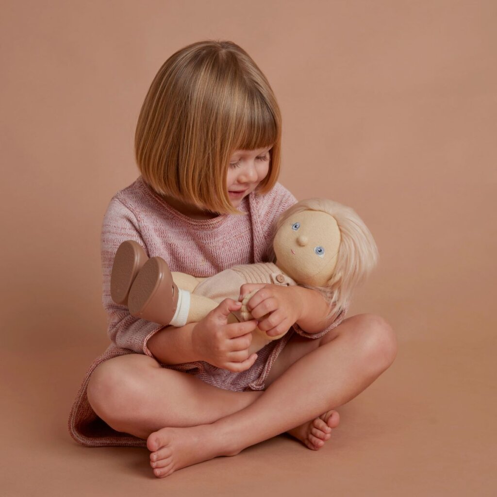 A child sat cross-legged holding Dinkum Doll Petal in their lap