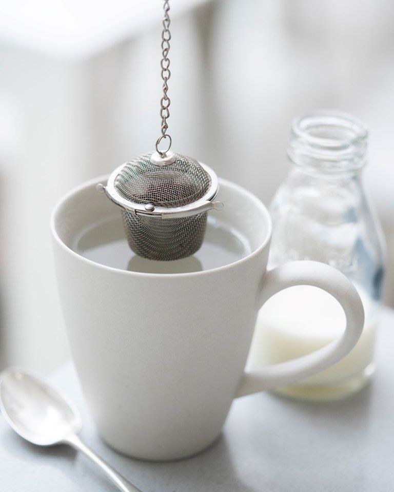 Ecoliving stainless steel loose tea infuser with a white mug and tea spoon.