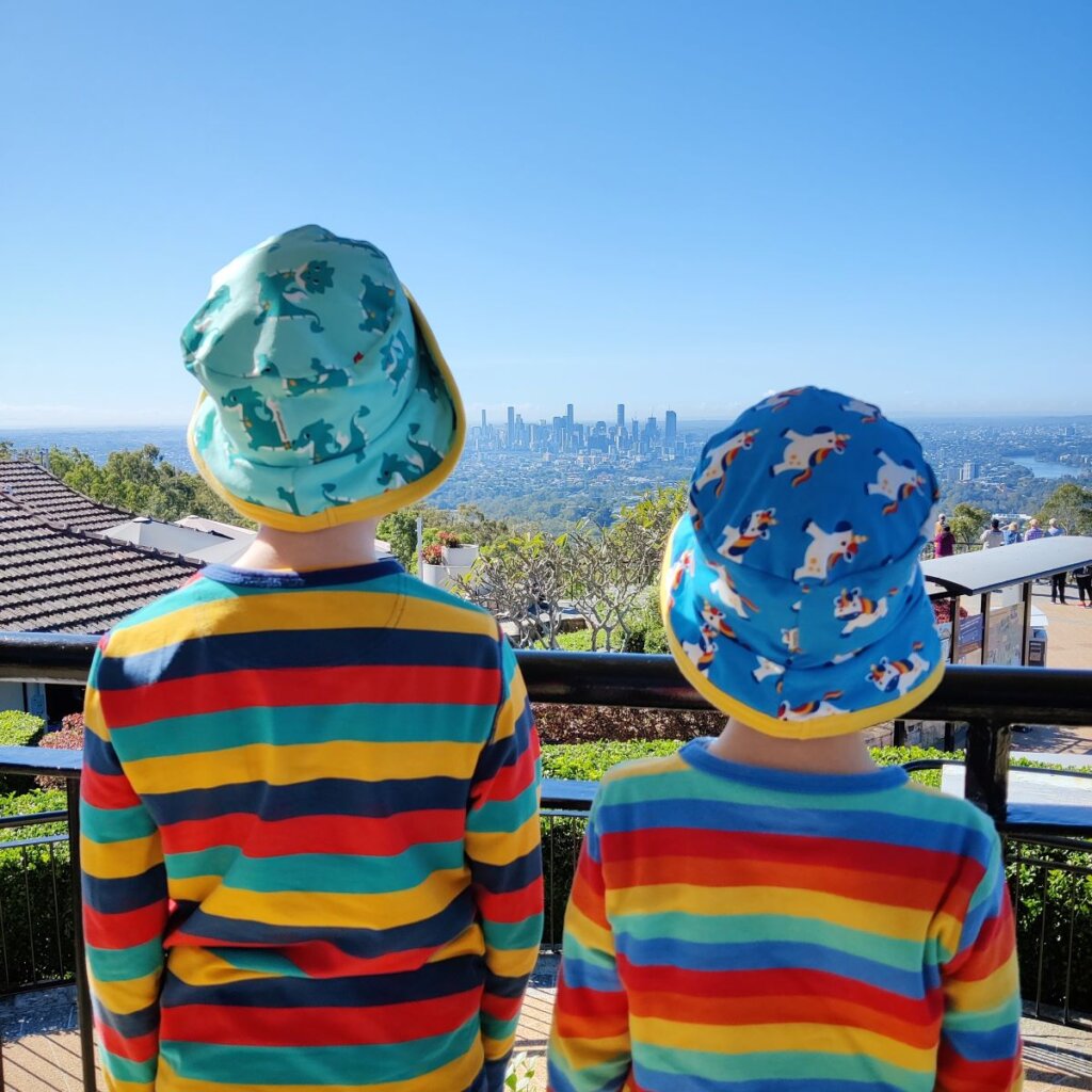 Two children look out across a city skyline wearing stripy tops and sun hats