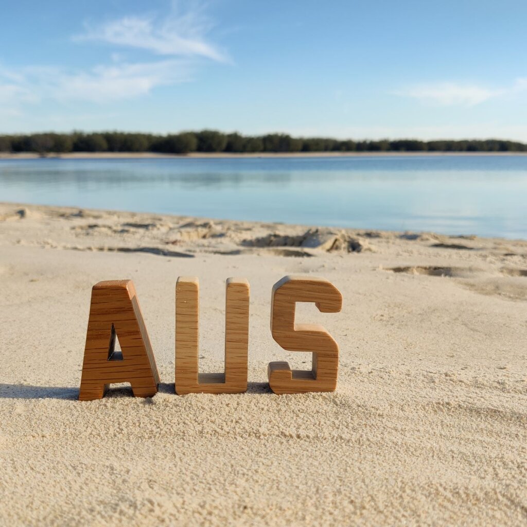 Reel Wood Capital Letters  spelling out AUS on a sandy beach with blue skies