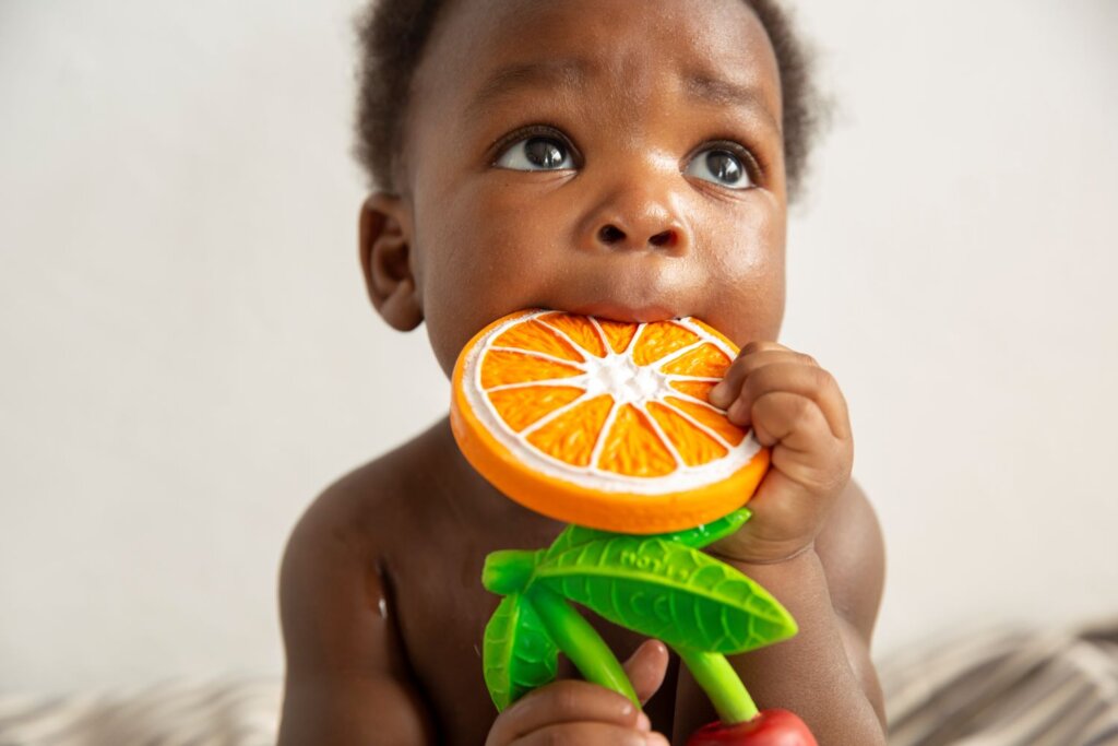 A baby holding the Oli & Carol Natural Rubber Baby Teether  Clementino the ORANGE