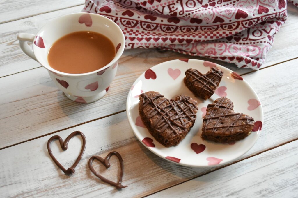 A cup of tea and heart-shaped chocolate biscuits on a heart decorated plate. 