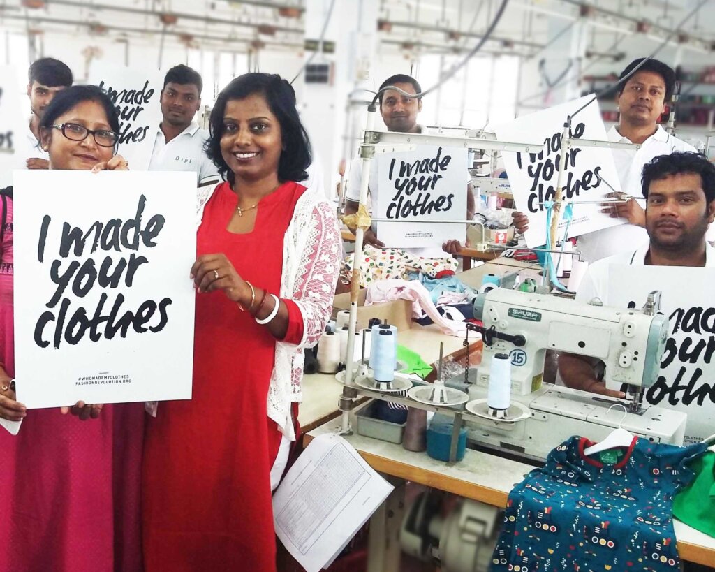 Textile producers at the Little Green Radicals factory holding up 'I Make Your Clothes' posters for Fashion Revolution Week